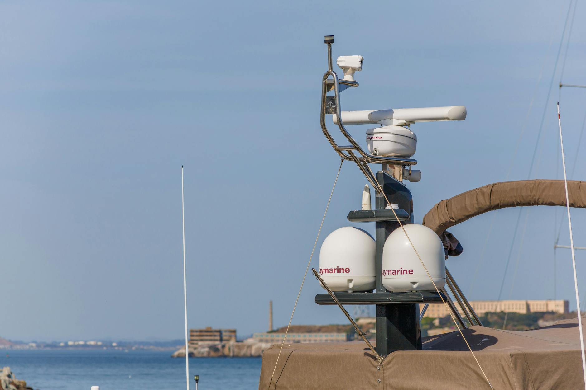 Close-up of radar navigation equipment on a yacht against a sunny coastal backdrop.