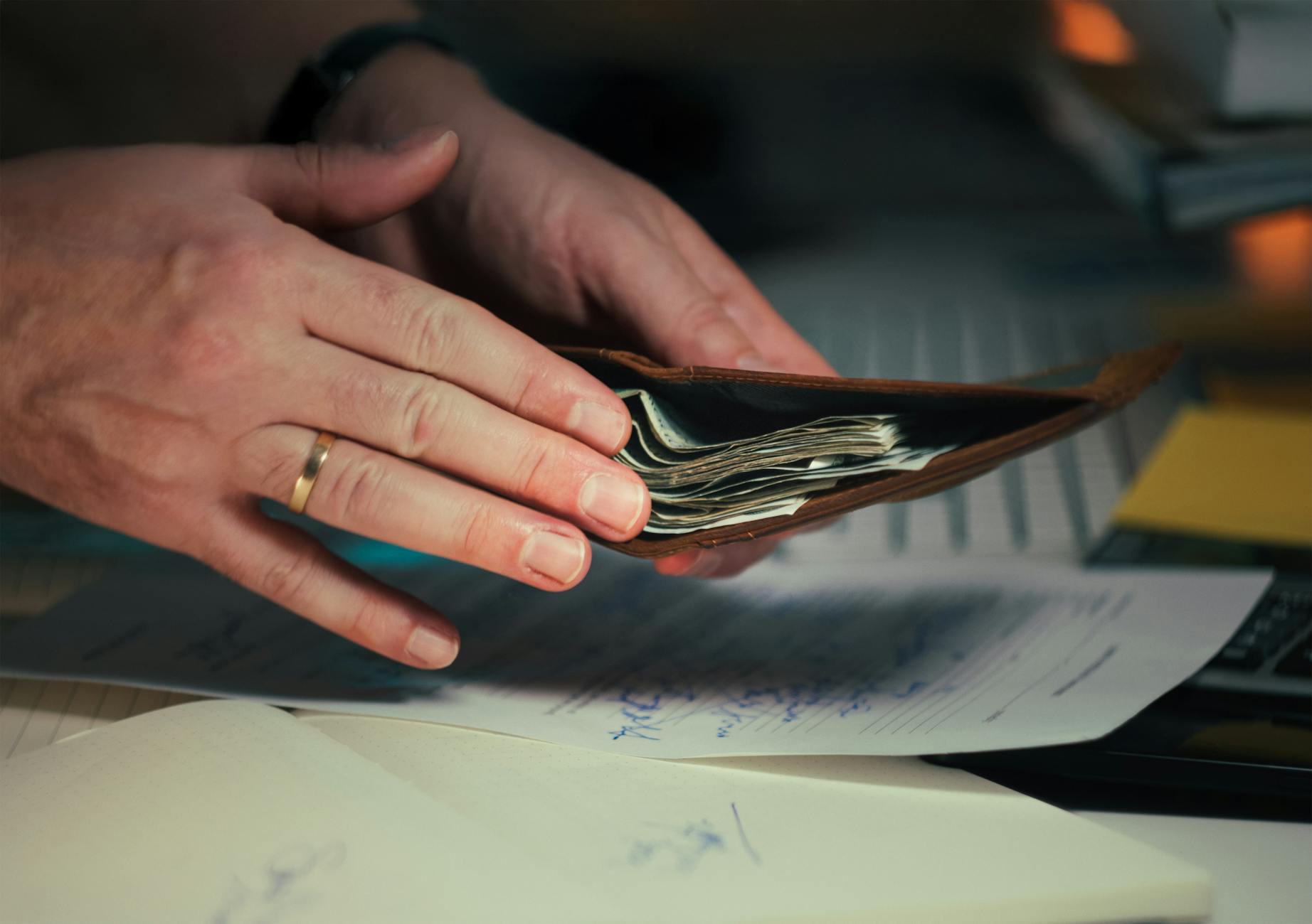 Hands holding an open wallet filled with cash above documents, indicating financial planning or budgeting.