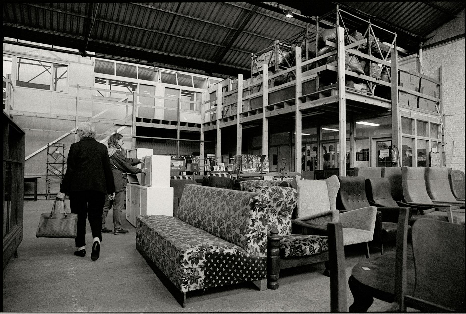 Monochrome view of a warehouse with two women browsing furniture.